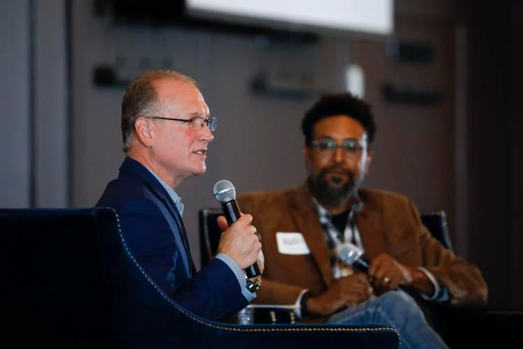 Two men speaking at a conference panel.