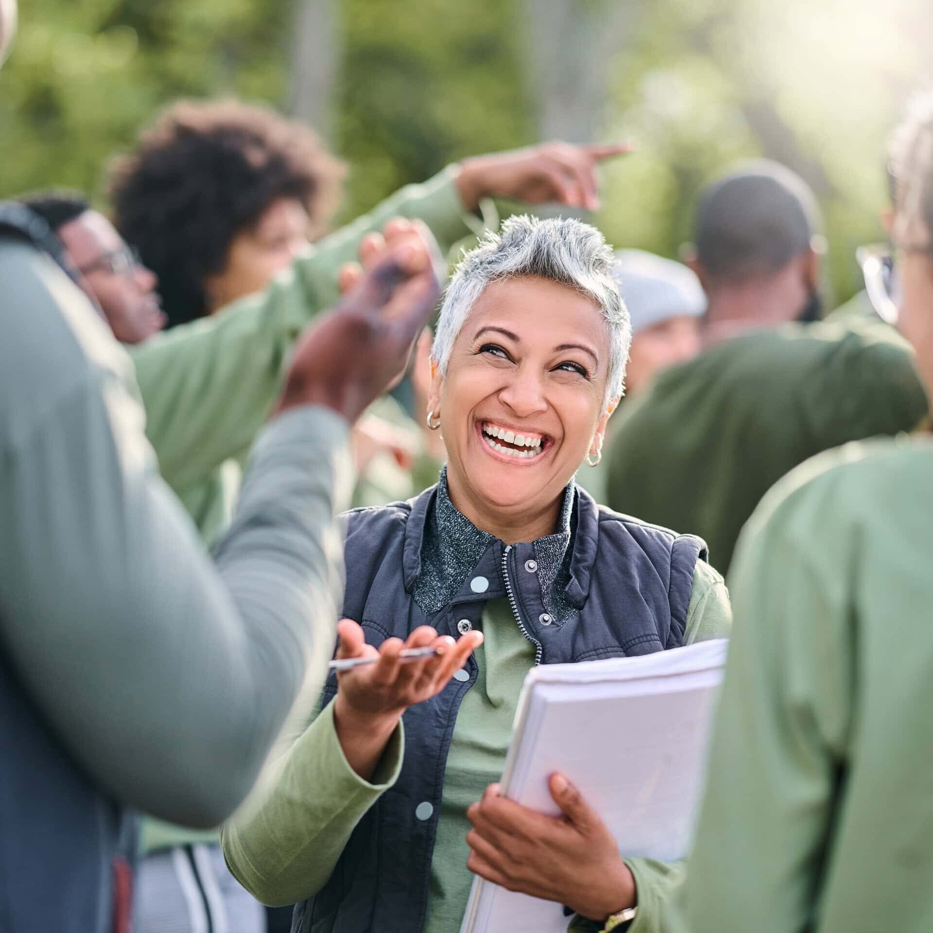 Volunteer, team and people in nature for community service, teamwork and planning with leadership, goals and strategy. Senior person or leader for management in forest, park or eco friendly project Smiling woman talking in group outdoors.